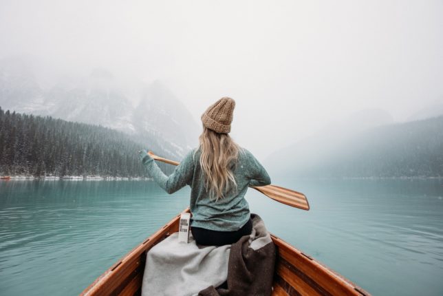 woman in gray long sleeve shirt sitting on brown wooden boat on body of water during