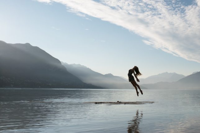 silhouette of jumping woman on raft in middle of lake