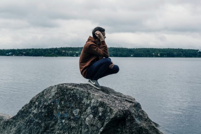 man wearing brown hoodie while standing on rock